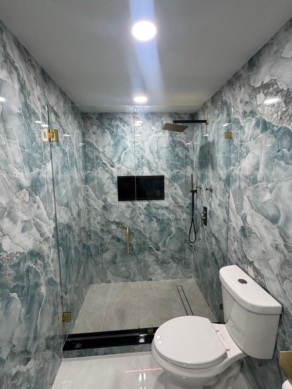 Ducha con mampara de cristal sin marco, herrajes dorados y paredes de mármol verde