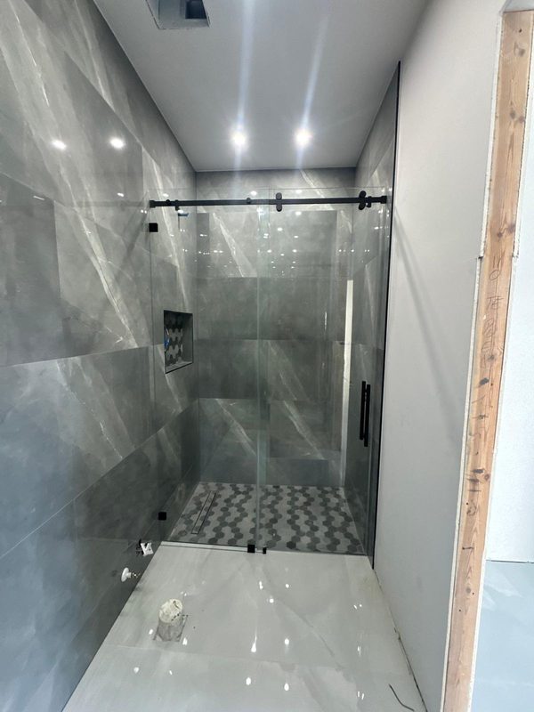 Mampara corredera de cristal con riel negro y paredes de porcelánico gris
