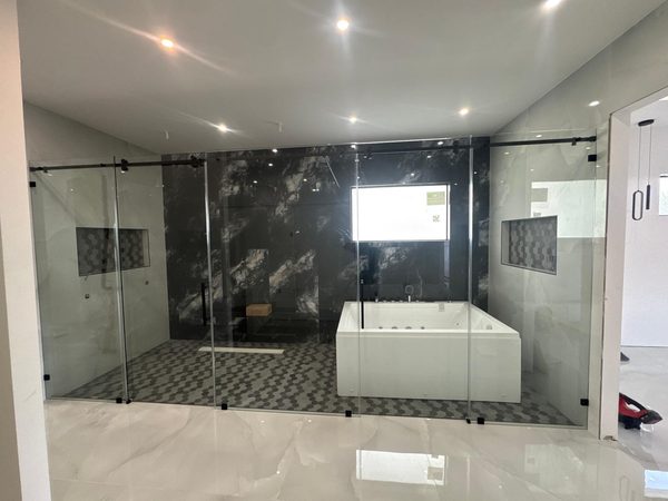 Gran cerramiento de cristal con herrajes negros que separa ducha y bañera