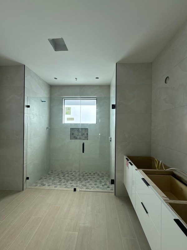 Frente de cristal con puerta y herrajes negros en un baño en obra